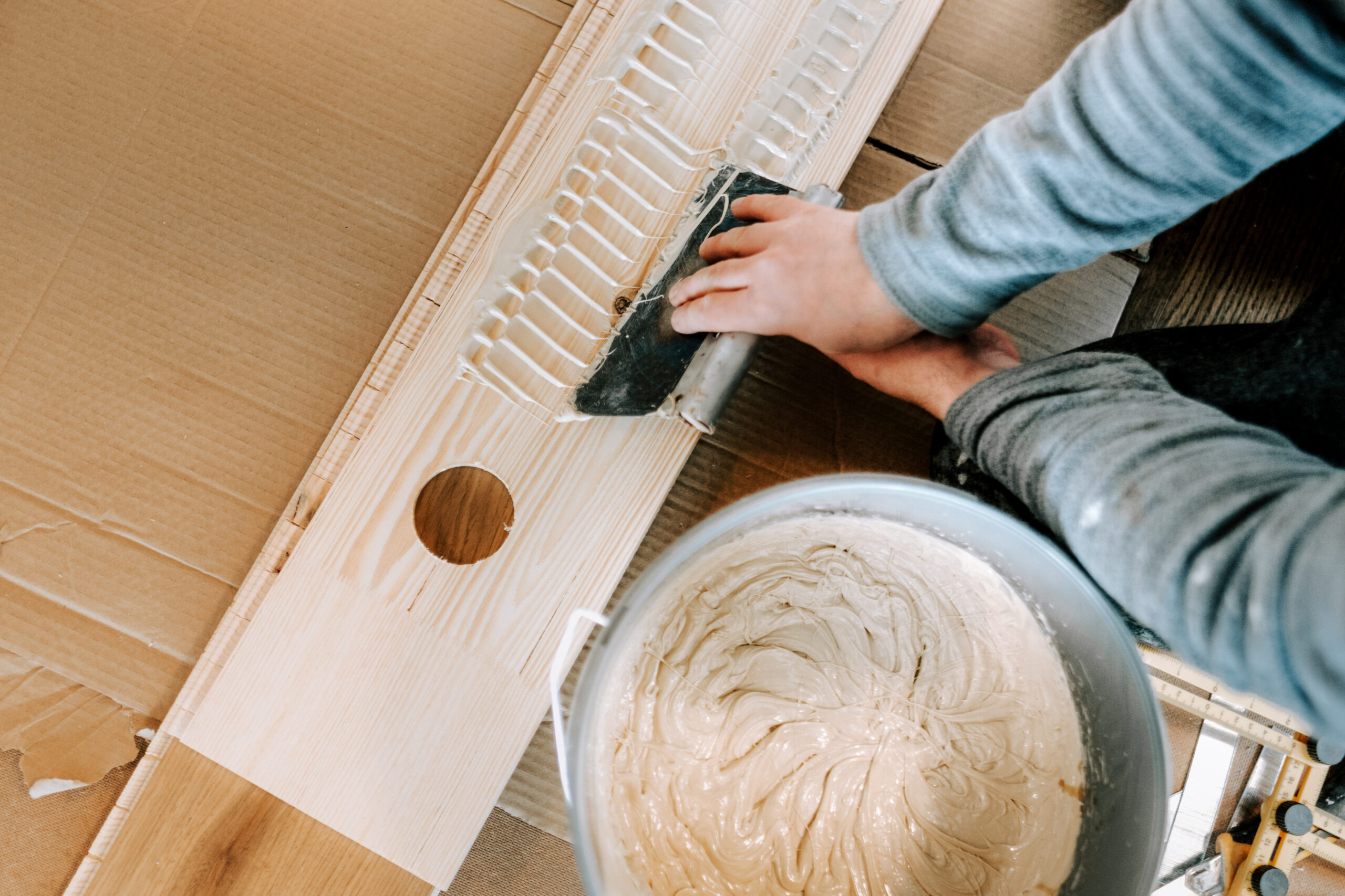 Installing wooden hardwood floor, detail on man hands holding wooden tile and spreading glue on parquet